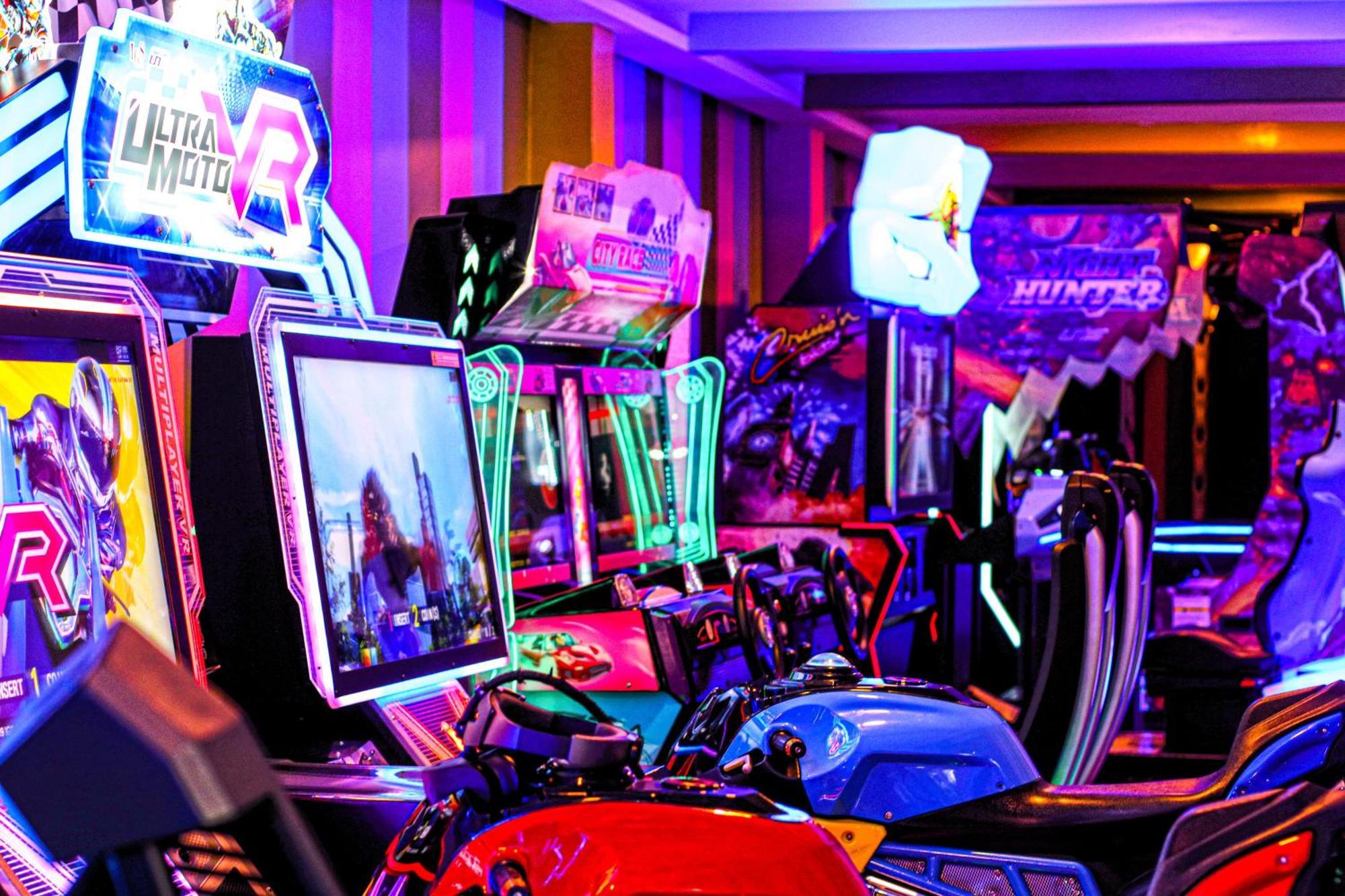 Lagoona Beach Luxury Resort And Spa Манама Экстерьер фото The photo shows a vibrant arcade scene featuring various arcade gaming machines. The machines are lined up, showcasing colorful screens and bright, neon lights, creating an energetic atmosphere. Some machines appear to be racing games, as indicated b