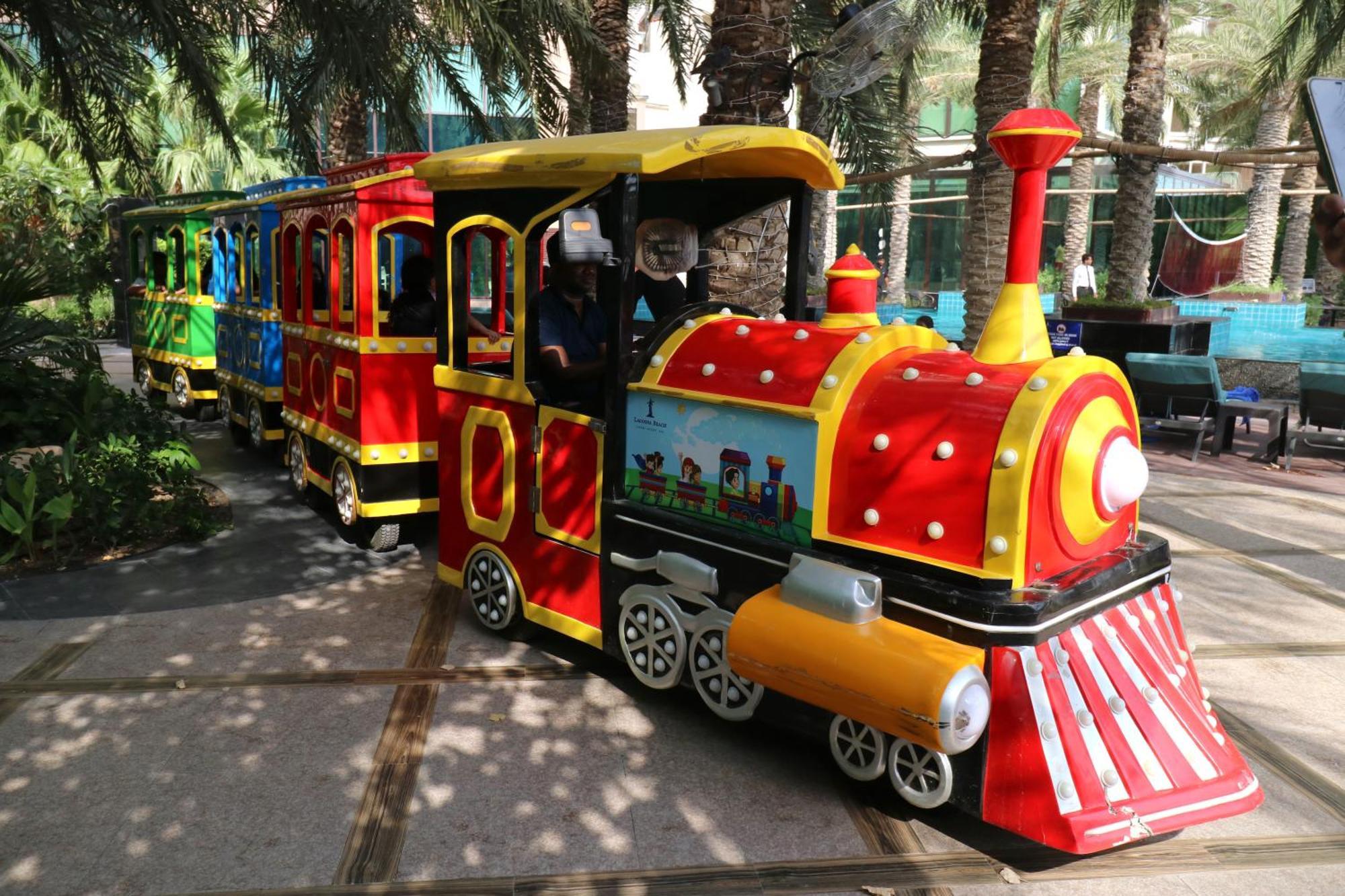 Lagoona Beach Luxury Resort And Spa Манама Экстерьер фото The photo shows a colorful miniature train. It features a vibrant design with bright red, yellow, and blue colors. The front of the train resembles a classic steam engine, complete with a prominent smokestack. The train is designed to resemble a fun 